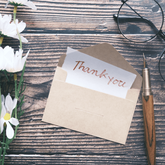 "Thank you!" letter on a desk with eye glasses, flowers and a fountain pen